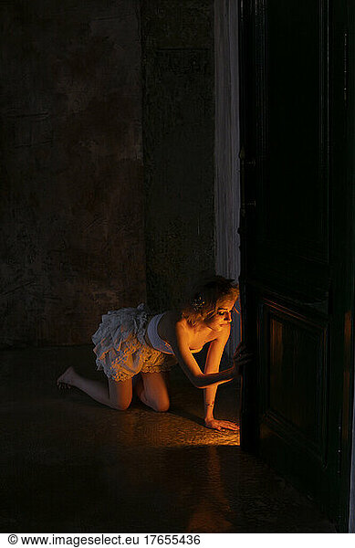Illuminated young woman kneeling in dark