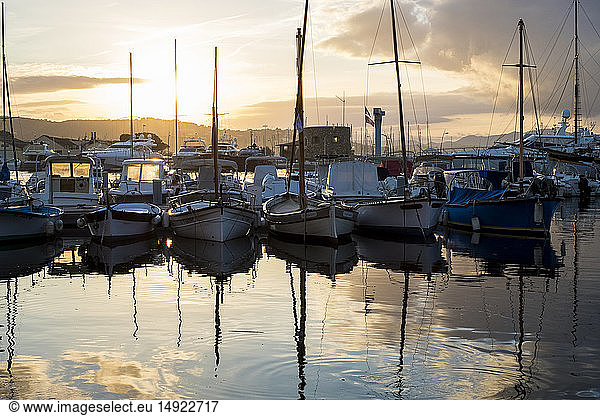Im Hafen vertäute Segelboote spiegeln sich bei Sonnenuntergang in ruhiger See.