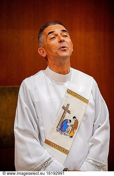 Im hinteren Teil einer katholischen Kirche in Südkalifornien singt ein Diakon in einer weißen Kutte während einer Messe zusammen mit Gemeindemitgliedern ein Kirchenlied.
