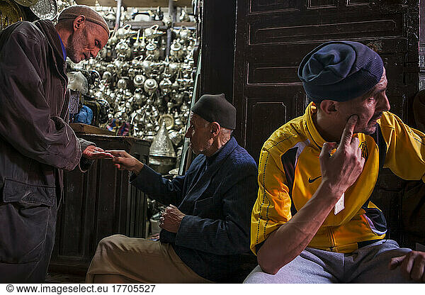 In der alten Medina von Fes  Marokko  gibt es Hunderte von Geschäften  die lokale Waren verkaufen. Hinter einem nachdenklichen Mann diskutieren zwei Herren über den Preis einer kostbaren Silberware; Fes  Marokko