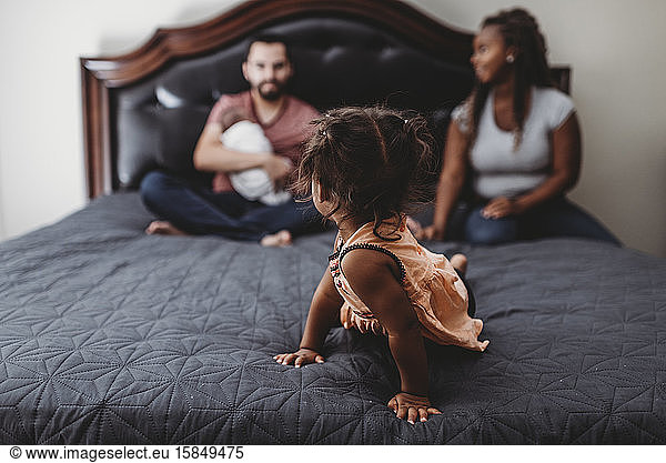 In-focus multiracial girl on bed looking back at blurry family