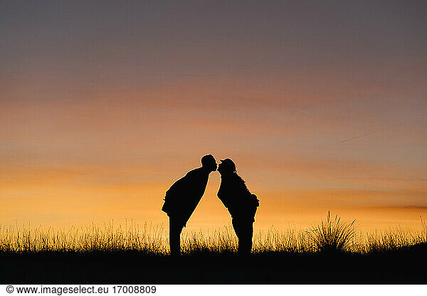 In silhouette of boyfriend and girlfriend kissing while standing against sky