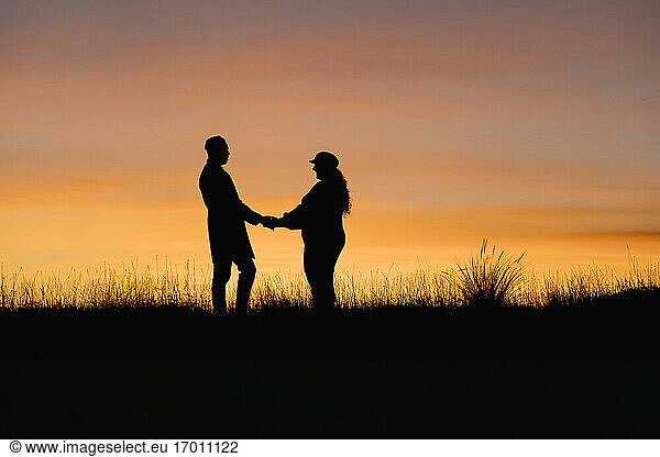 In silhouette of man and woman holding hands while standing against sky
