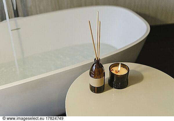 Incense sticks by burning scented candle on table near bathtub