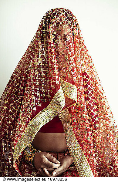 Indian bride looks out from under traditional red veil before wedding
