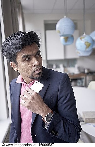 Indian man at home peering backwards at world globes  thinking about getting away from it all