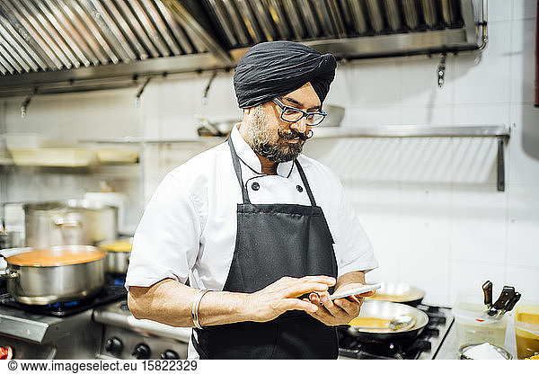 Indischer Küchenchef benutzt Smartphone in Restaurantküche