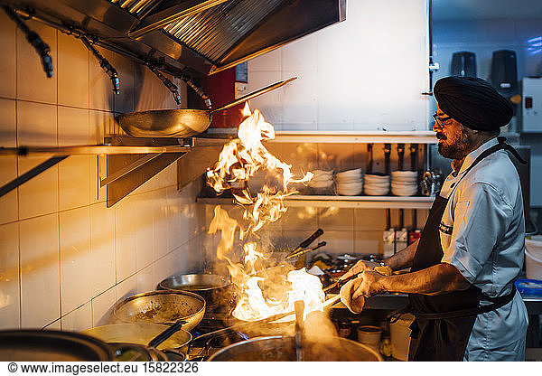 Indischer Koch brennt Essen in Restaurantküche an