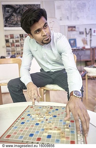 Indischer Mann spielt Puzzle-Brettspiel mit Buchstaben  Sprachenlernen