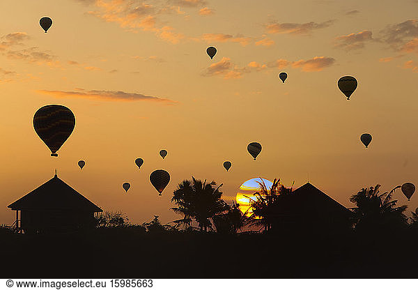 Indonesia  Bali  Silhouettes of hot air balloons flying over coastal huts at moody sunset