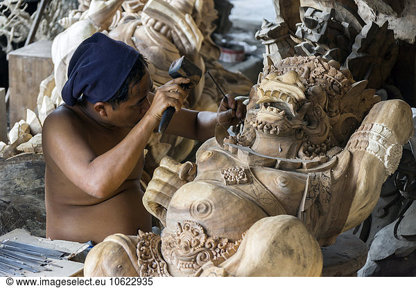 Indonesia  Bali  Ubud  Traditional wood carver's workshop with man working on religious wood sculptures