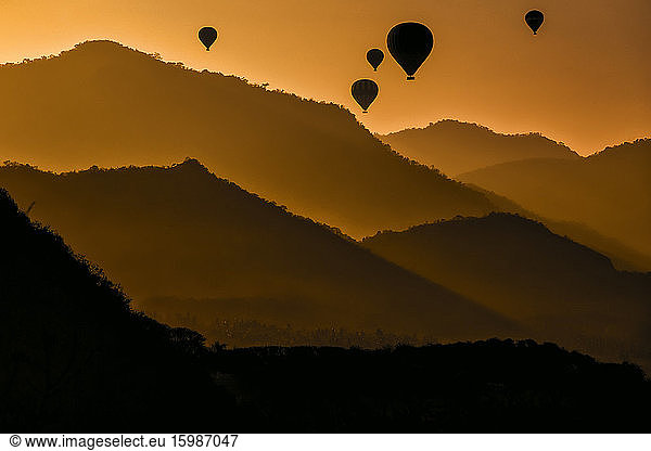 Indonesia  West Nusa Tenggara  Silhouettes of hot air balloons flying over Sumbawa island at moody dusk