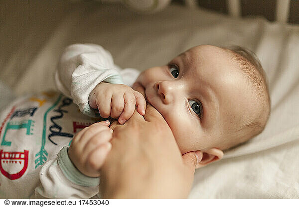 Infant baby biting hand of mother while teething