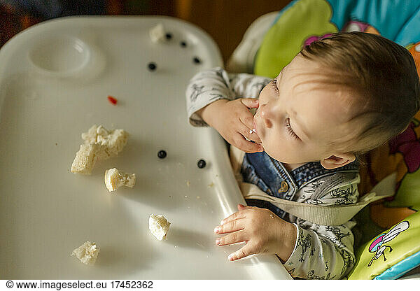 Infant boy sitting in baby chair learning how to eat independent