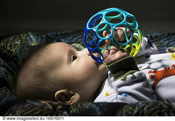 Infant in pajama lying and playing with colorful ball in dark room