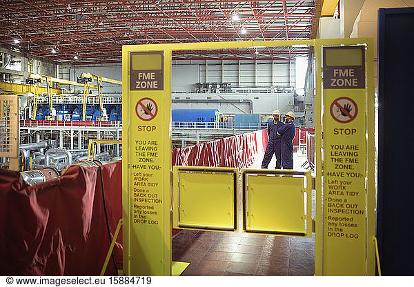 Ingenieure  die auf einem Portal an einer Absperrung und großen Warnschildern in einer Sperrzone für Fremdmaterial in einem Kernkraftwerk stehen