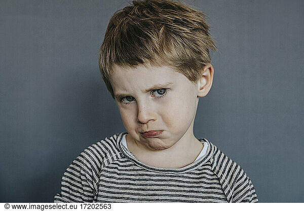 Innocent boy making face on gray background