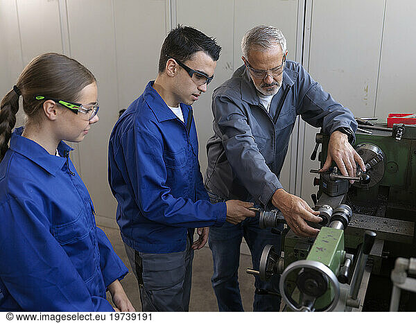 Instructor guiding apprentices using lathe at workshop