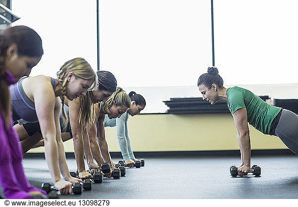 Instructor guiding women in doing push-ups with dumbbells at gym