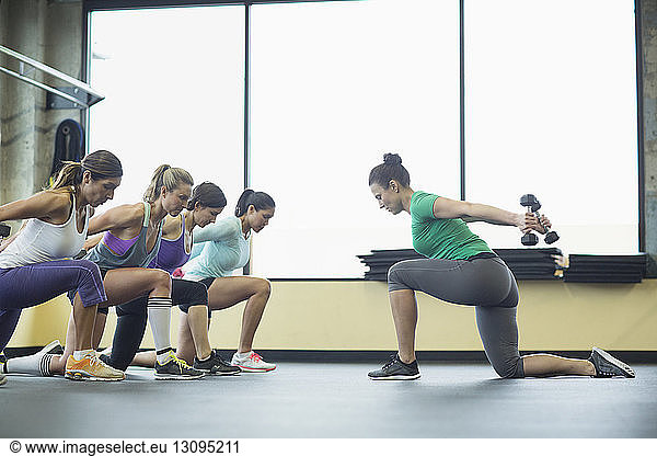 Instructor guiding women in exercising with dumbbells at health club