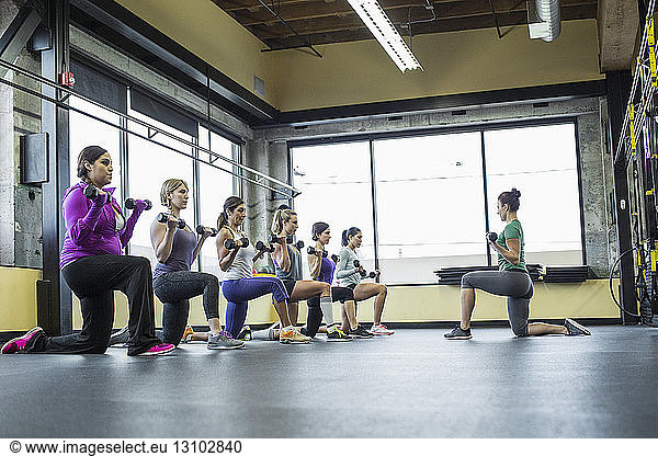 Instructor guiding women in lifting dumbbells at gym