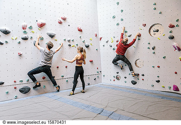 Instructor training male and female students rock climbing in gym