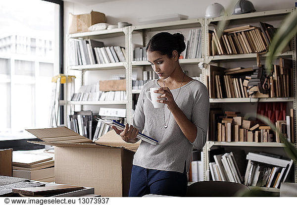 Interior designer holding coffee mug while examining files in office