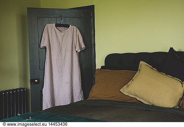Interior view of bedroom with light green walls  double bed with and pale pink linen nightgown on hanger over door.