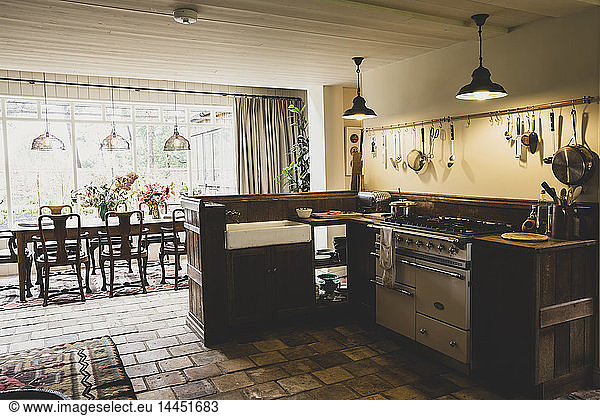 Interior view of kitchen with stone tile floor  range cooker and butler's sink  open plan to conservatory with antique wooden dining table and chairs.