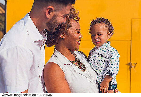 Interracial family of three smiling in front of yellow wall
