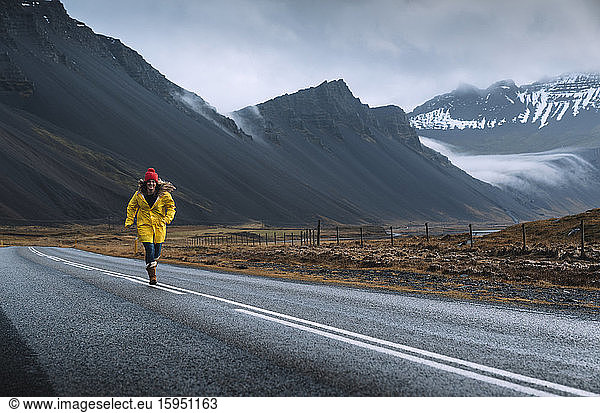 Island  Frau in gelbem Mantel läuft entlang der abgelegenen isländischen Autobahn