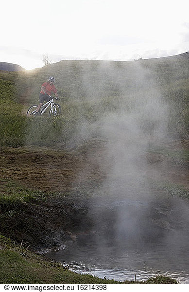 Island  Mountainbiker mit Blick auf eine heiße Quelle
