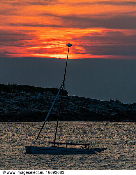 Isolated sailboat as the sun sets beyond clouds in the distance.