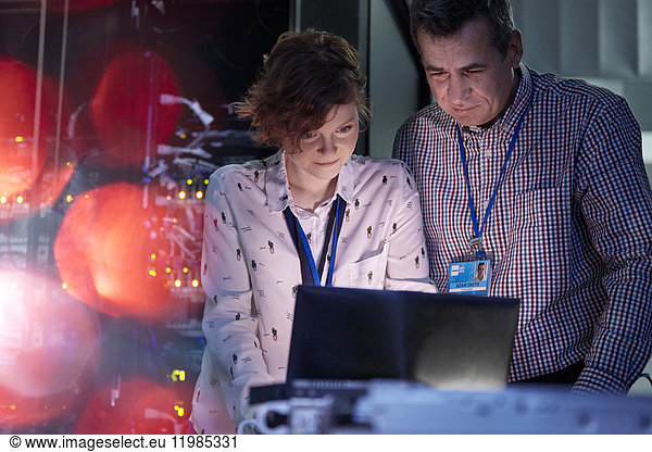 IT technicians working at laptop in dark server room