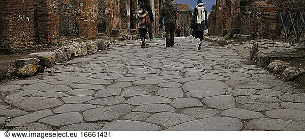 Italien. Pompeji. Touristen gehen durch die gepflasterte Straße.
