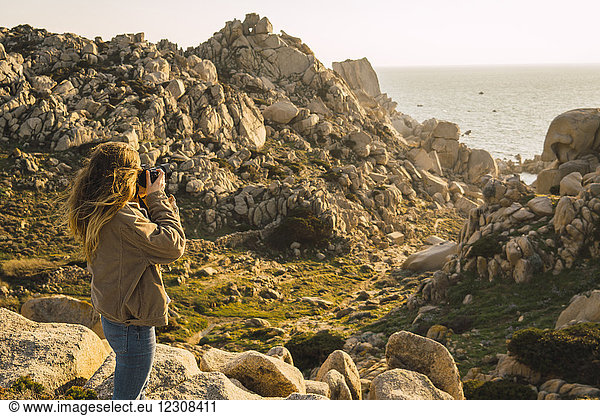 Italien  Sardinien  Frau auf einer Wanderung  die ein Foto an der Küste macht.