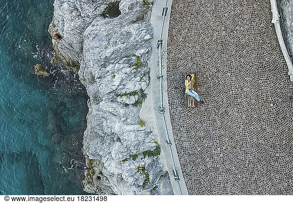 Italy  Apulia  Erchie  Aerial view of young woman lying on bench overlooking Amalfi Coast