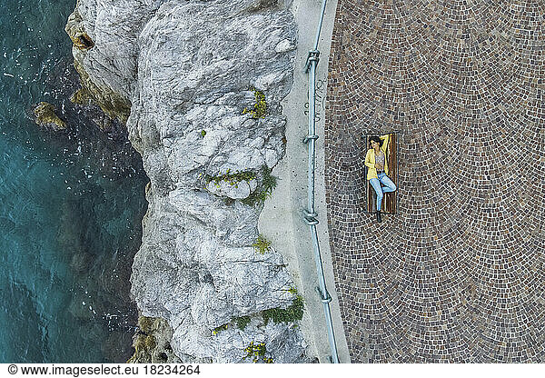 Italy  Apulia  Erchie  Aerial view of young woman lying on bench overlooking Amalfi Coast