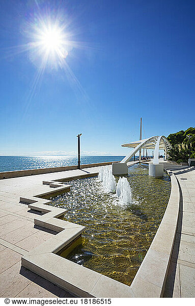 Italy  Friuli Venezia Giulia  Grado  Sun shining over modern promenade fountain