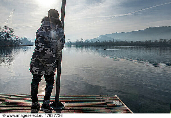 Italy  Rear view of boy  on pier on calm lake
