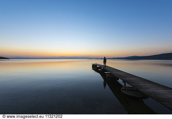 Italy  Umbria  Lake Trasimeno  silhouette of man standing on jetty watching sunset