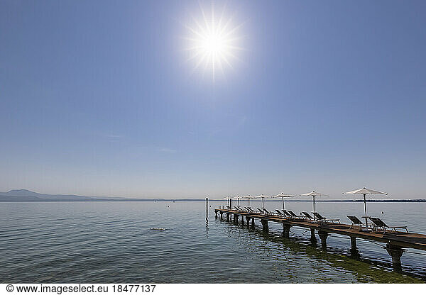 Italy  Veneto  Bardolino  Sun shining over deck chairs and umbrellas on lakeshore jetty