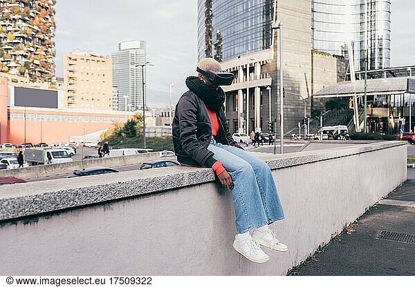 Italy  Woman withVRgoggles sitting on wall in city