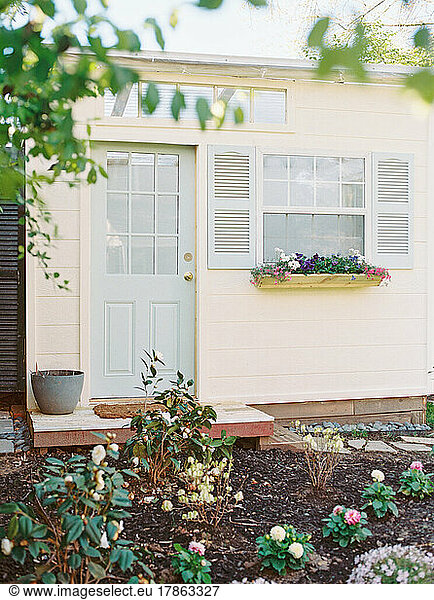 Ivory shed with light blue door and shutters and flowers