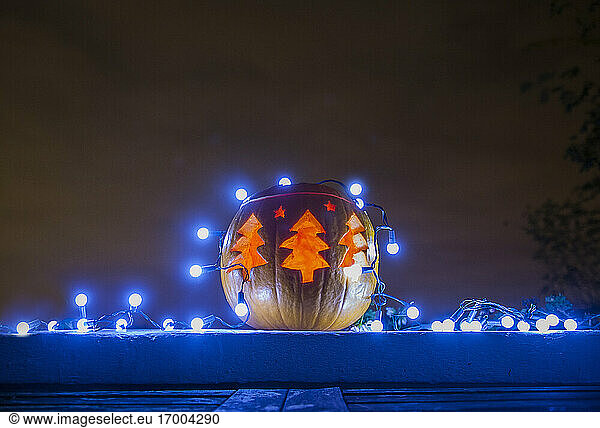 Jack o lantern decorated with blue Christmas lights glowing outdoors at night