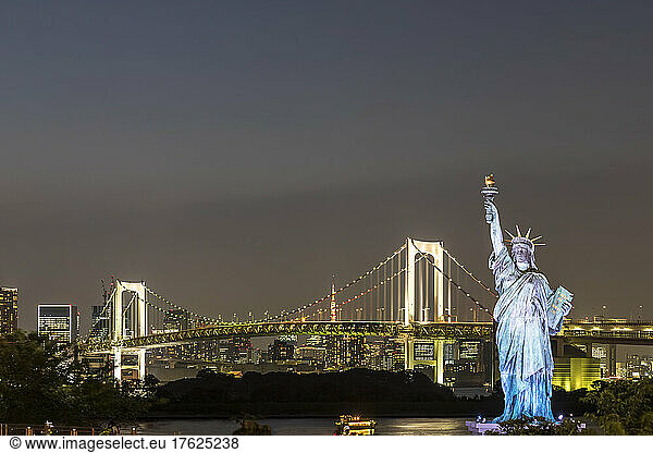 Japan  Kanto Region  Tokyo  Replica of Statue of Liberty and illuminated Rainbow Bridge at night
