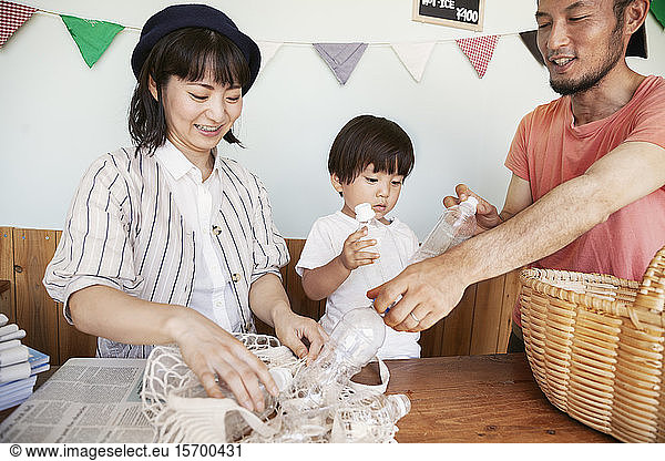 Japanese man,  woman and boy standing in a farm shop,  sorting clear plastic bottles into basket.