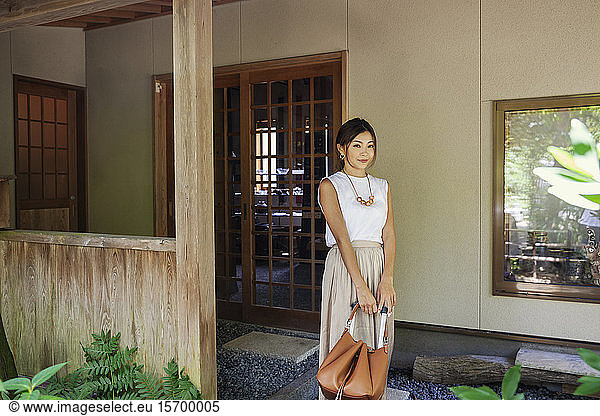 Japanische Frau steht auf einer Veranda und hält eine Handtasche.