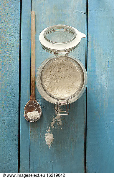Jar of flour with wooden spoon on table