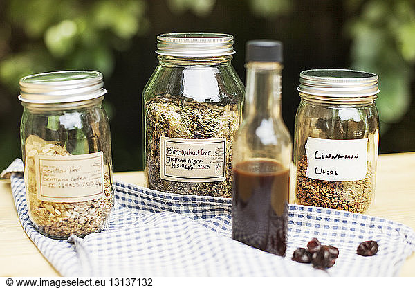 Jars of spices with syrup bottle and cloth on wooden table